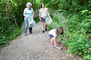 Little girl, pregnant mother and grandmother cleaning the forest of plastics