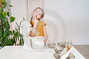 little girl prepares dough in a submersible mixer and licks his fingers