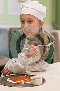 Little girl preparing homemade pizza. Beautiful little girl in a chef attire with a pizza in her hands. vertical photo