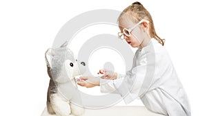 Little girl preschooler disguised as a doctor plays with a plush dog in a veterinary clinic and gives it an injection with a