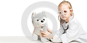 Little girl preschooler disguised as a doctor wearing glasses plays with a plush dog in a veterinary clinic and listening to a toy