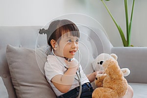 Little girl pretending to be doctor while treating her stuffed toy with stethoscope on sofa in living room at home