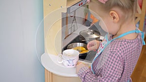 A little girl pretending to cook with a wooden kitchen set. Imaginative play with a miniature wooden stove and pots.