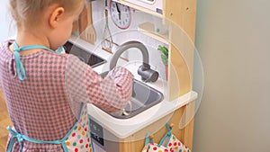 A little girl pretending to cook with a wooden kitchen set. Imaginative play with a miniature wooden stove and pots.