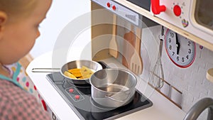 A little girl pretending to cook with a wooden kitchen set. Imaginative play with a miniature wooden stove and pots.