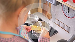 A little girl pretending to cook with a wooden kitchen set. Imaginative play with a miniature wooden stove and pots.