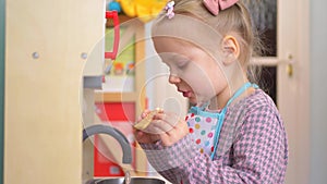 A little girl pretending to cook with a wooden kitchen set. Imaginative play with a miniature wooden stove and pots.