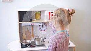 A little girl pretending to cook with a wooden kitchen set. Imaginative play with a miniature wooden stove and pots.