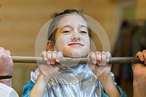 Little girl pulling herself up on a wooden crossbar