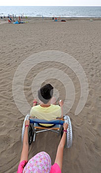 little girl pushes a special wheelchair on the sandy beach with