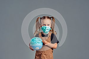 Little girl put a gauze mask on an globe. The concept of protection against coronavirus infections covid-19