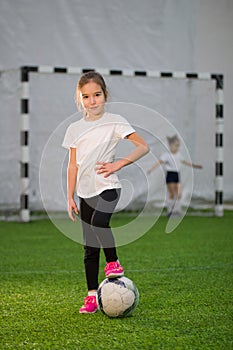 A little girl put her foot on the ball on the football field, smiling and looking at the camera
