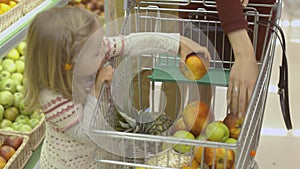 Little girl puts fruits in the trolley