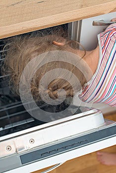 Little girl putting head into dishwasher.