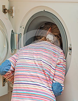 Little girl putting head into washing machine.