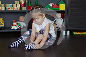 Little girl putting on socks sitting on floor indoor