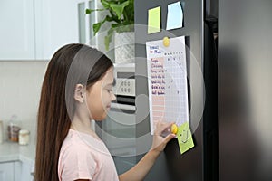 Little girl putting to do list on fridge