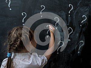 Little girl with question marks on blackboard. Concept for confusion, brainstorming and choice.