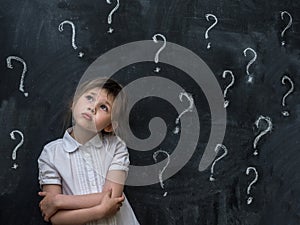 Little girl with question marks on blackboard. Concept for confusion, brainstorming and choice.