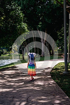 A little girl in a rainbow dress fun running on the concrete path in the park