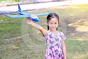 Little girl raise up a blue toy airplane flying on air in the garden outdoor