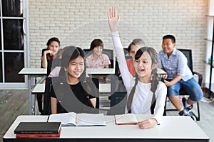 Little girl raising hands in classroom education concept