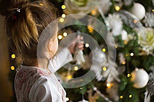 A little girl reaches for a Christmas tree toy with her hand. Christmas decor, waiting for a holiday and a miracle. New Year. Whit