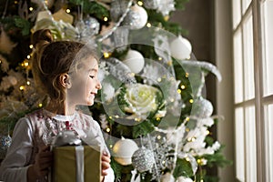 A little girl reaches for a Christmas tree toy with her hand. Christmas decor, waiting for a holiday and a miracle. New Year. Whit