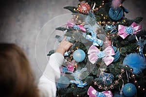 A little girl reaches for a Christmas tree toy with her hand. Christmas decor, waiting for a holiday and a miracle. New Year. Whit