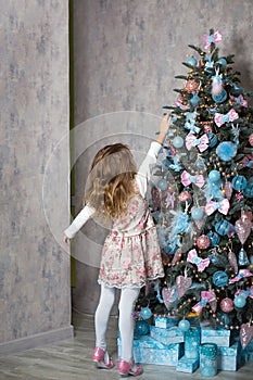 A little girl reaches for a Christmas tree toy with her hand. Christmas decor, waiting for a holiday and a miracle. New Year. Whit