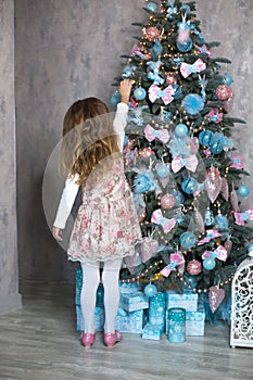 A little girl reaches for a Christmas tree toy with her hand. Christmas decor, waiting for a holiday and a miracle. New Year. Whit