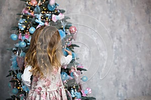 A little girl reaches for a Christmas tree toy with her hand. Christmas decor, waiting for a holiday and a miracle. New Year. Whit