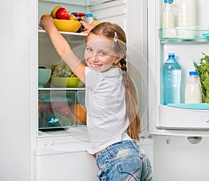 Little girl reaching apples in fridge