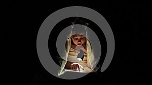 Little girl is read a book under a blanket with a flashlight