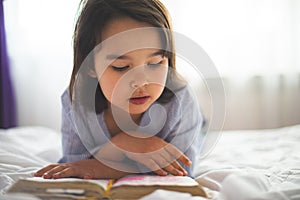 Little girl reading from bible while she is in bed in the morning