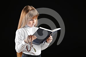 Little girl reading Bible on dark background