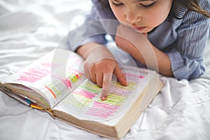 Little girl reading from Bible while lying in bed. Fetita citind din biblie in timp ce sta intinsa in pat