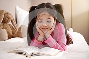 Little girl reading book on bed