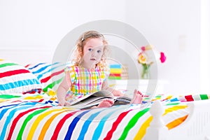 Little girl reading a book in bed