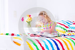 Little girl reading a book in bed