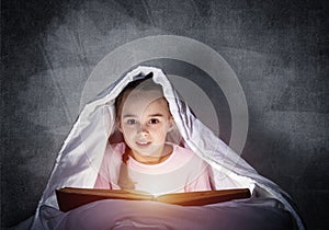 Little girl reading book in bed