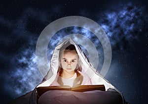 Little girl reading book in bed