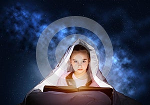 Little girl reading book in bed