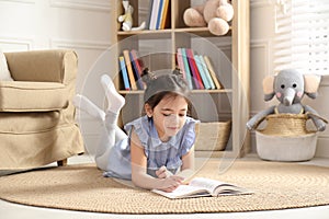 Little girl reading book on floor at home