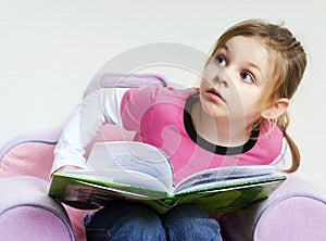 Little girl reading a book and looking up