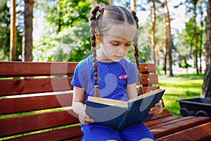 Little girl reading a book in the outdoors.