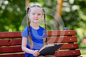 Little girl reading a book outdoors.