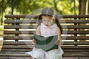 Little girl reading a book sitting on a bench in the garden