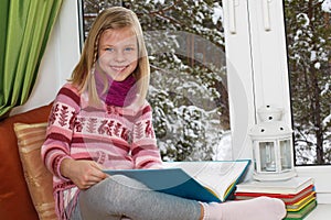 Little girl reading a book sitting on the window on Christm photo