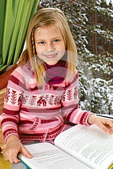 Little girl reading a book sitting on the window on Christm photo